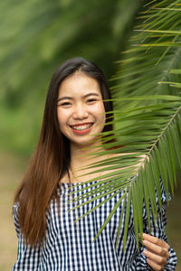 Portrait of smiling young woman standing by plant outdoors