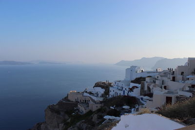 Buildings by sea against clear blue sky