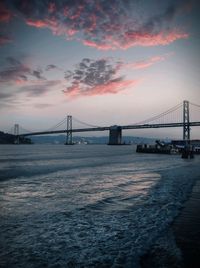 Suspension bridge over sea against sky during sunset