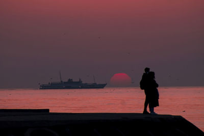 Rear view of silhouette woman standing at beach against sky during sunset