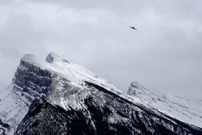 Low angle view of airplane flying over snowcapped mountain against sky