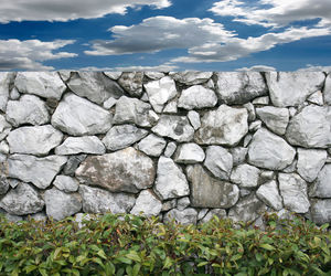 Stone wall by rocks against sky