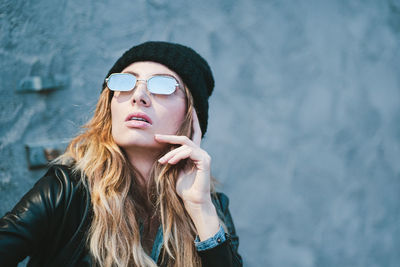 Portrait of young woman wearing sunglasses against wall