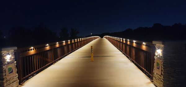 Illuminated footbridge against clear sky at night