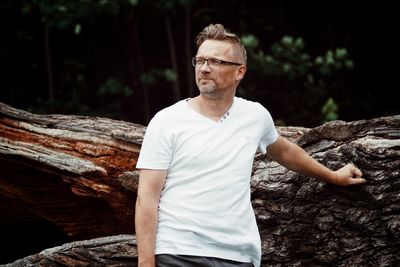 Thoughtful mature man standing by log in forest