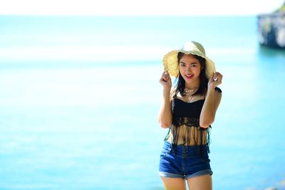Young woman wearing hat standing against sea