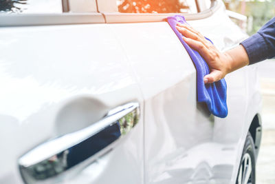 Cropped hand of man cleaning car with blue towel