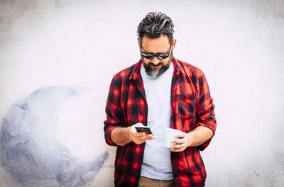 Young man using mobile phone while standing against wall