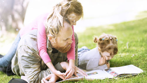 Picture of father and two daughters on weadow reading a book. outdoors parents and children.