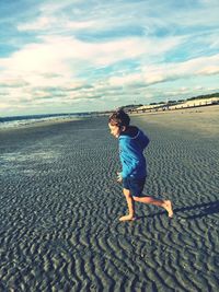 Boy standing on sand at beach against sky