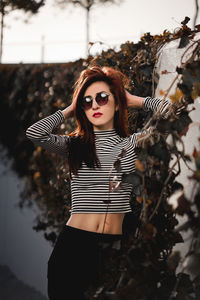 Portrait of young woman wearing sunglasses while standing by wall
