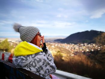 Side view of woman yawning against sky during winter