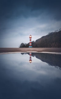 Reflection of lighthouse in lake against sky