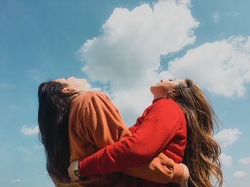 Cheerful friends embracing while standing against sky