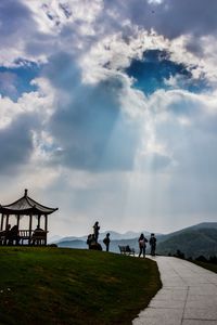 People at riverbank against cloudy sky