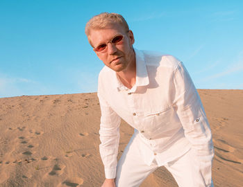 Young man standing at desert against clear blue sky