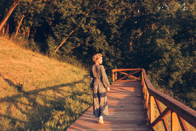 Woman walking on footbridge against trees