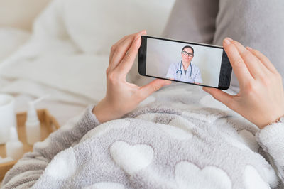 Midsection of woman using mobile phone on bed at home