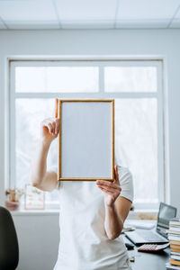 Midsection of woman reading book while standing against window