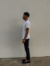 Side view of young man looking away against wall