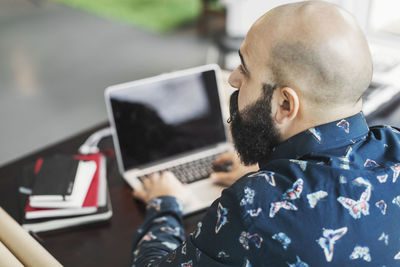 Rear view of male architect looking away while using laptop at table