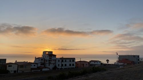 Buildings by sea against sky during sunset