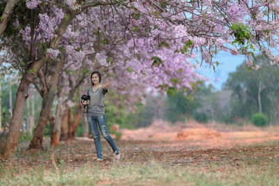 Portrait of woman with camera standing on field against trees