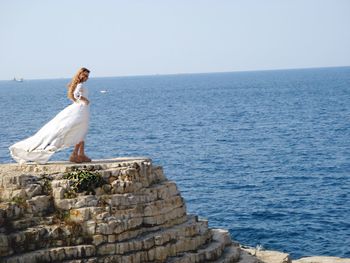 Woman in dress standing at sea against clear sky