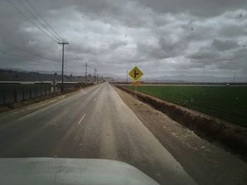 Road passing through field against cloudy sky