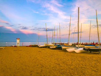 Sailboats moored on beach against sky during sunset