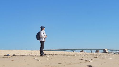 Side view full length of woman standing at sandy beach against clear blue sky