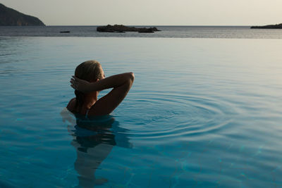 Woman in infinity pool by sea during sunset