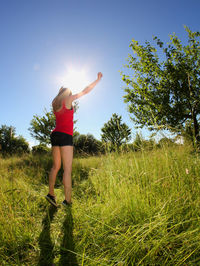 Full length of beautiful woman with arms raised standing on grassy field