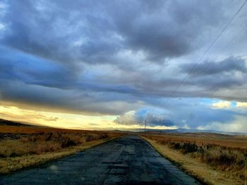 Road passing through landscape against storm clouds