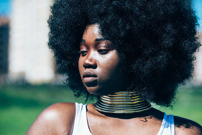 Young black woman in authentic golden necklace and afro hairstyle looking away on blurred background of countryside