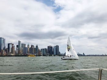 Sailboats in sea by buildings against sky