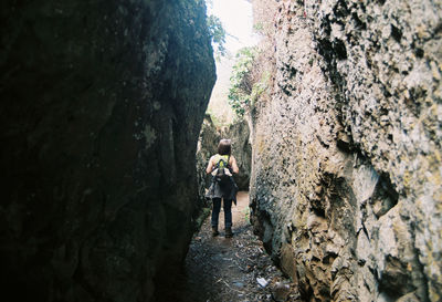 Full length rear view of woman walking on narrow alley amidst rock formations