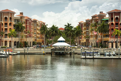 Buildings by river against sky in city