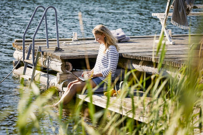 Mid adult female using laptop while sitting on jetty during summer