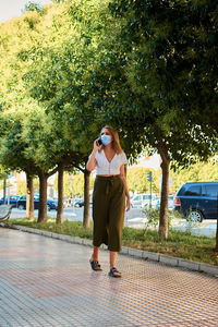 Woman talks on the phone while walking down the street wearing a mask