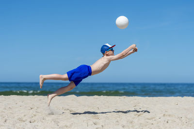 Full length of boy playing volleyball against sea
