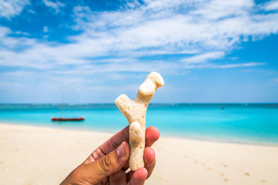 Hand holding sand on beach against sky