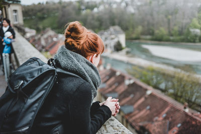 Side view of young woman with backpack standing by retaining wall