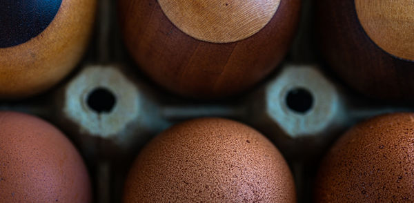 Three fresh eggs close to three wooden eggsmade of pear, oak, wenge and maple wood.