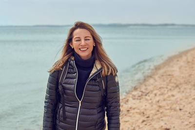 Cheerful woman wearing warm clothing standing at beach