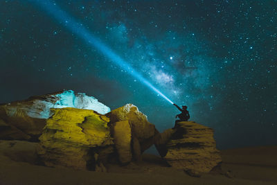 Rear view of man standing on rock at night