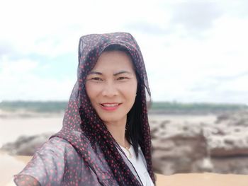 Portrait of smiling young woman on beach against sky