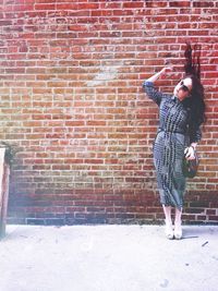 Woman tossing hair while standing against brick wall