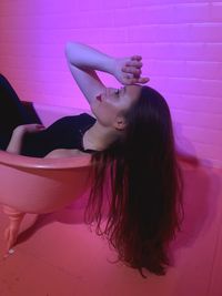 Thoughtful young woman reclining on pink chair