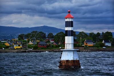 Lighthouse amidst sea and buildings against sky